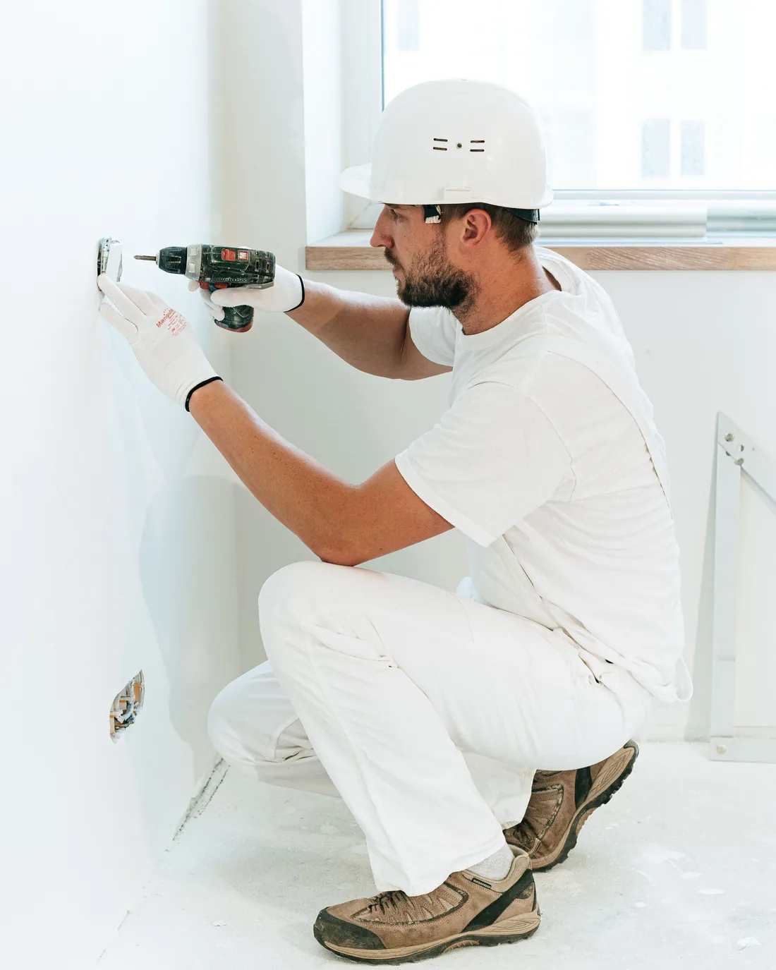 Un électricien pose une prise dans une pièce blanche.