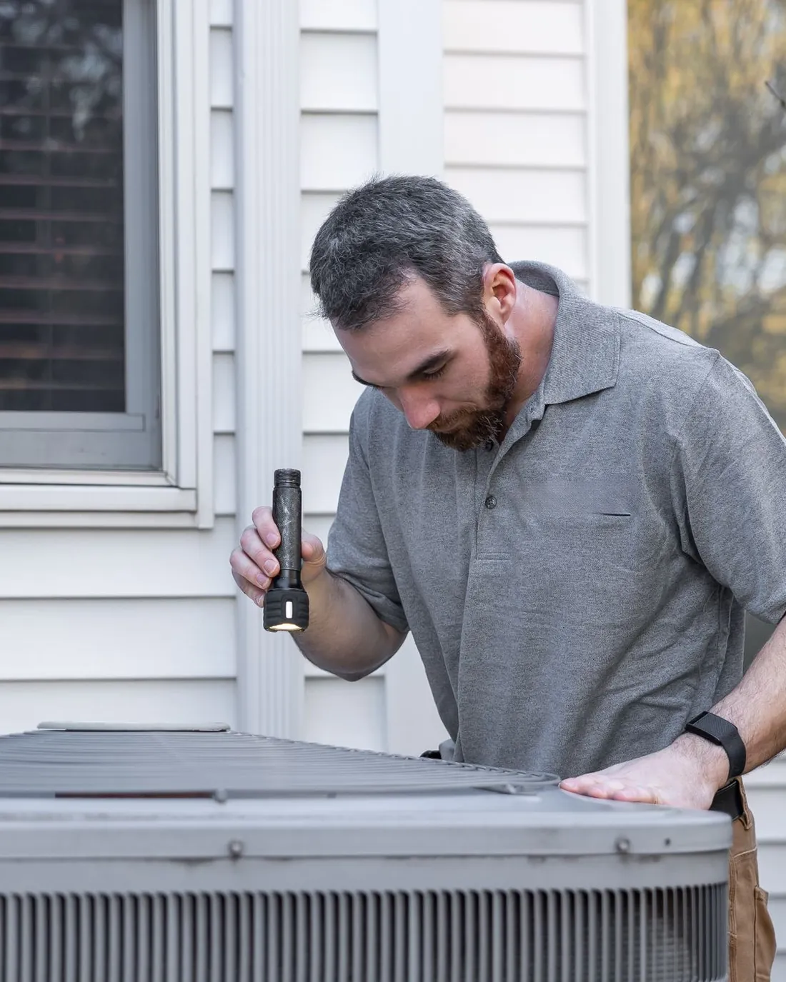 Un technicien contrôle une unité de climatisation devant une maison.